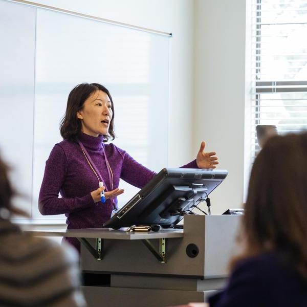 An economics major professor lectures her class at a podium.