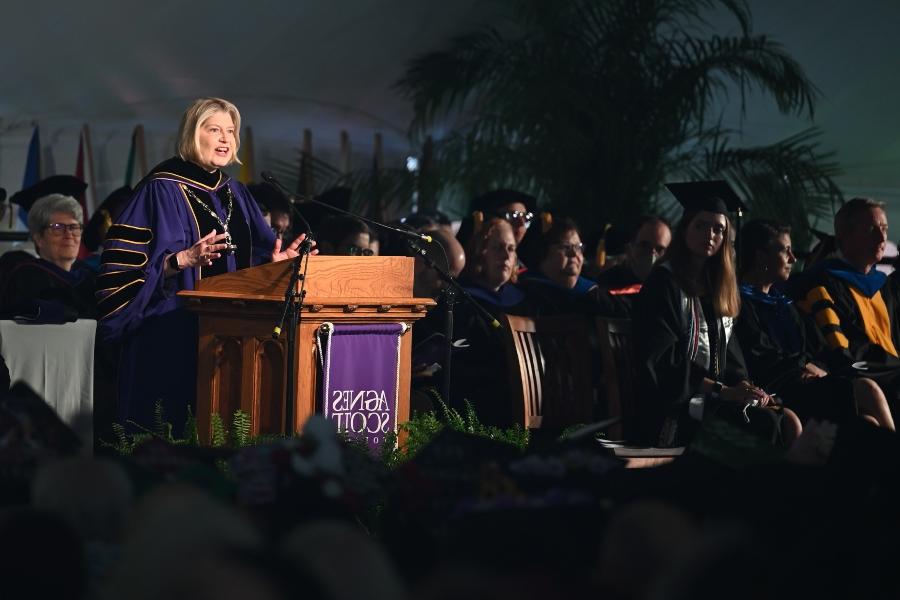 A spotlight focus on a college president in purple and black robe. 